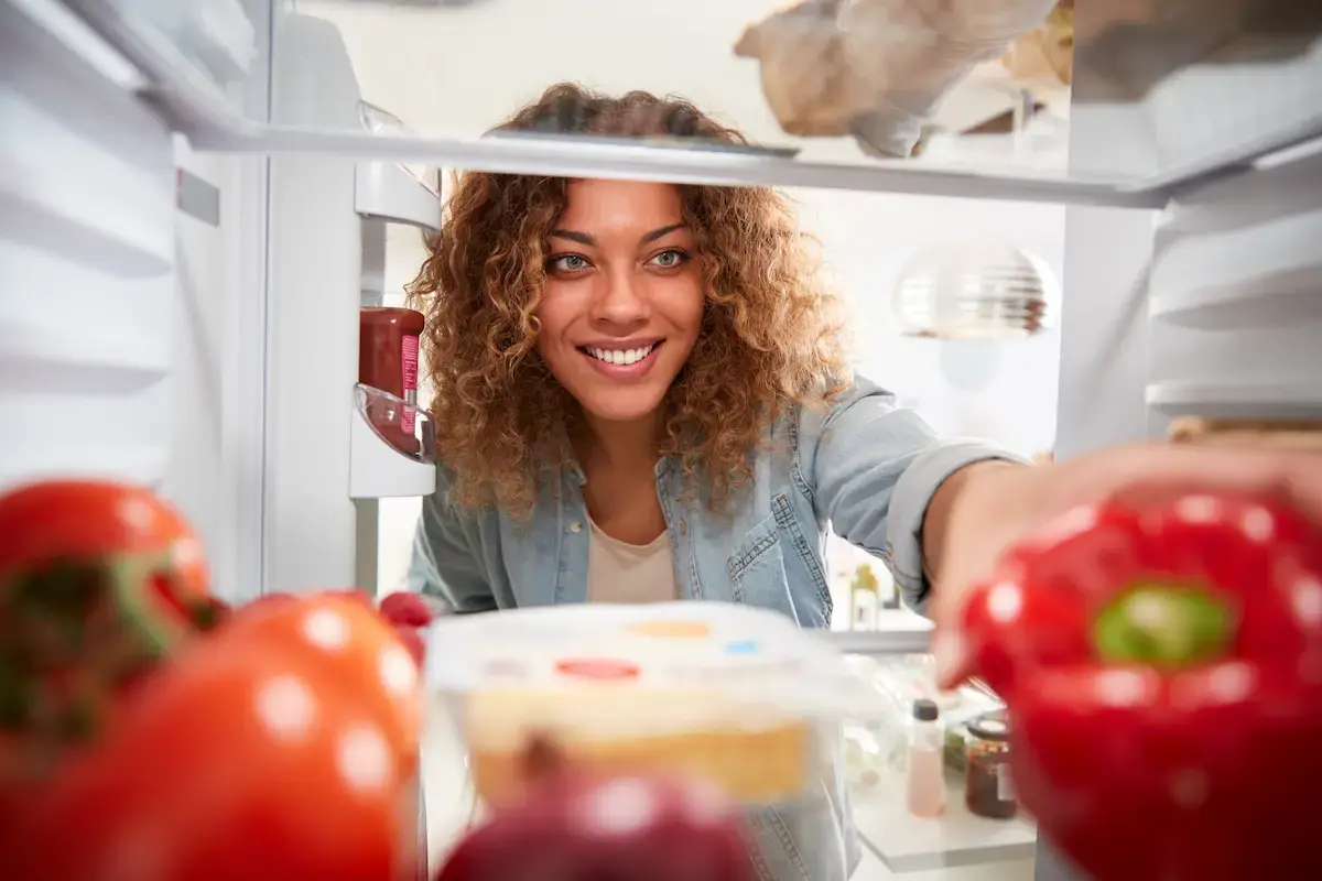 Woman reaching in the fridge for a bell pepper