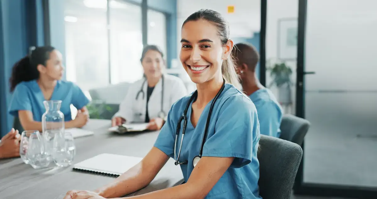 Nurse sitting at a board table with other healthcare professionals, smiling